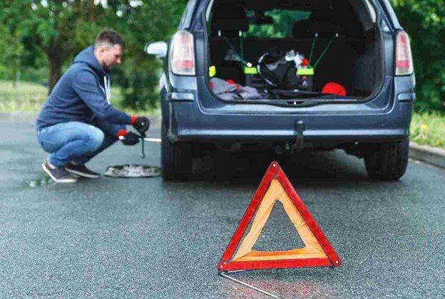 Driver waiting safely on the roadside with a broken-down car.