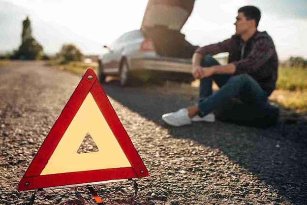 Driver waiting safely on the roadside with a warning triangle placed behind a broken-down car.