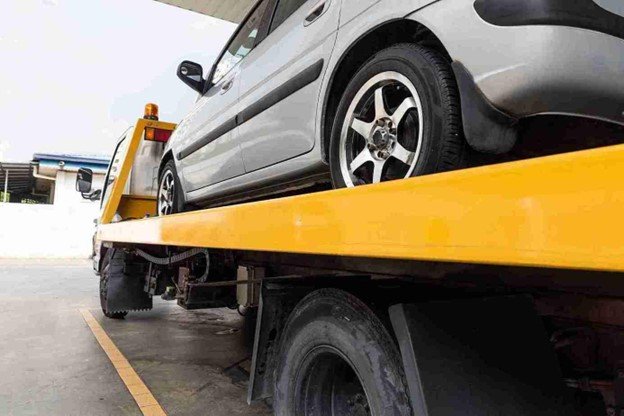 Tow truck operator securing a car on a flatbed using towing equipment