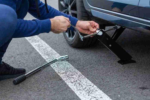 Man using a lug wrench to loosen wheel nuts during a step-by-step tire change process on the roadside