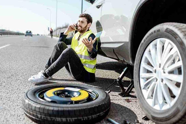 Man using a lug wrench to loosen wheel nuts during a step-by-step tire change process on the roadside