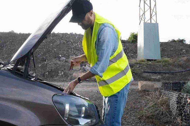 Roadside assistance worker checking engine oil level on a car with the hood open