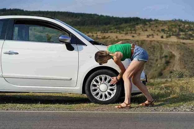 Woman checking a flat tire on a white car stopped along the roadside