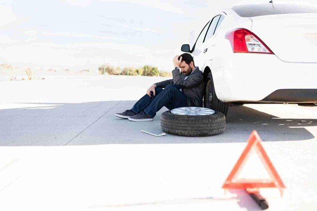 Driver sitting beside a car with a removed tire on the roadside