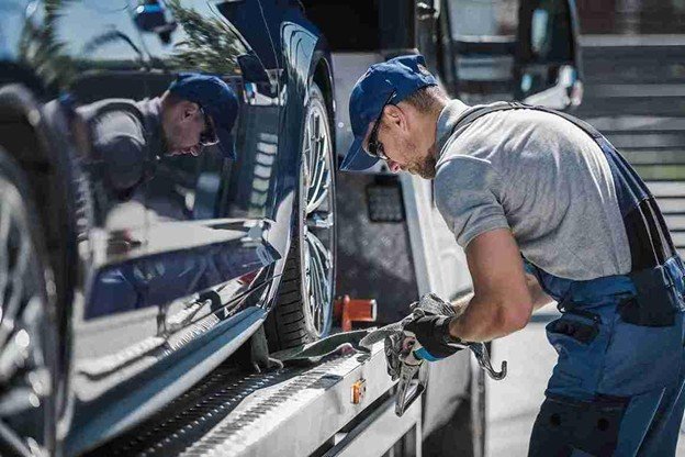 Tow truck operator standing beside a vehicle secured on a flatbed after roadside recovery
