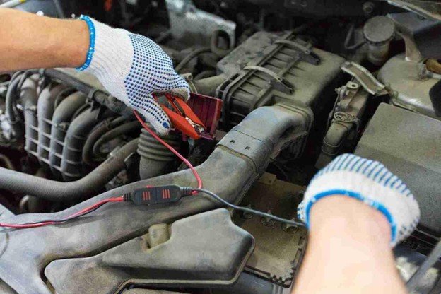 Gloved hands connecting jumper cables to a car battery inside the engine bay