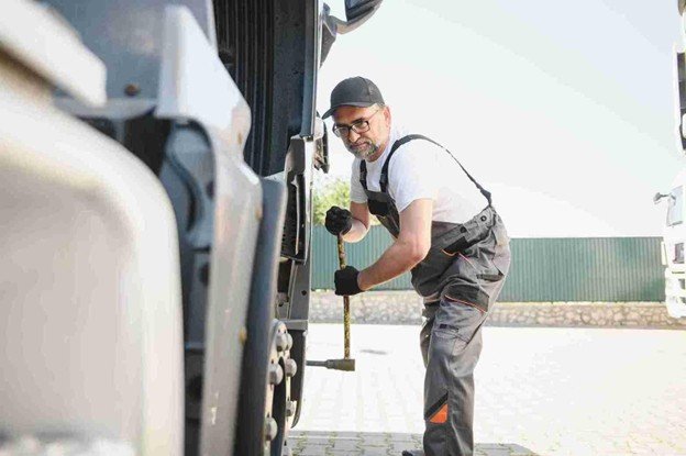 Tow truck operator using a hand crank to secure equipment on a service truck