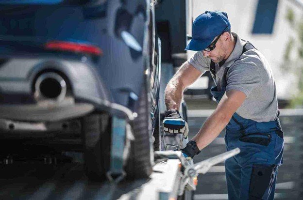 Tow truck operator securing a vehicle to a flatbed using chains and safety equipment