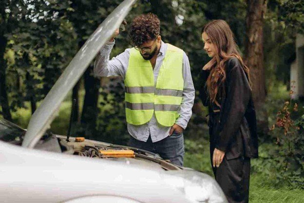 Roadside assistance worker inspecting a vehicle engine with the hood open while a driver stands nearby