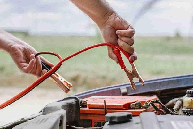 Close-up of hands holding jumper cable clamps above a car battery inside the engine bay