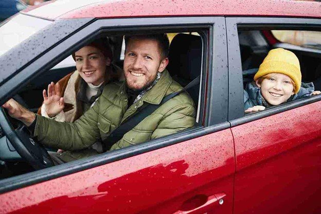Family smiling and waving from inside a red car during a safe and comfortable drive