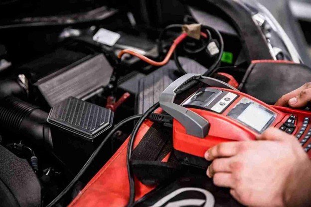 Close-up of a portable battery jump starter connected inside a vehicle engine bay
