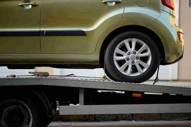 Side view of a small green car secured on a flatbed tow truck with wheel straps attached