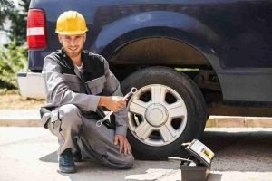 Mechanic kneeling beside a pickup truck holding a wrench next to a removed wheel