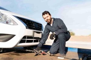 Tow truck operator attaching chains to a vehicle positioned on a flatbed for recovery
