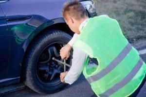 Roadside technician in a safety vest loosening lug nuts on a car tire