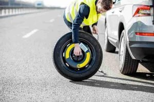 Technician kneeling on a freeway shoulder installing a temporary spare tire